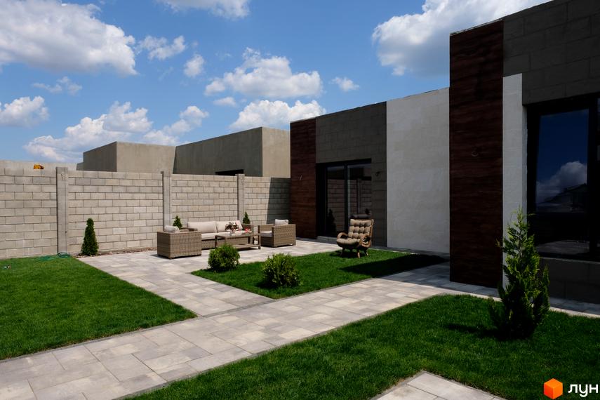 Зовнішній вигляд Котеджного містечка La Vida. Двоповерховий будинок з терасою та газоном. На території є меблі для відпочинку.