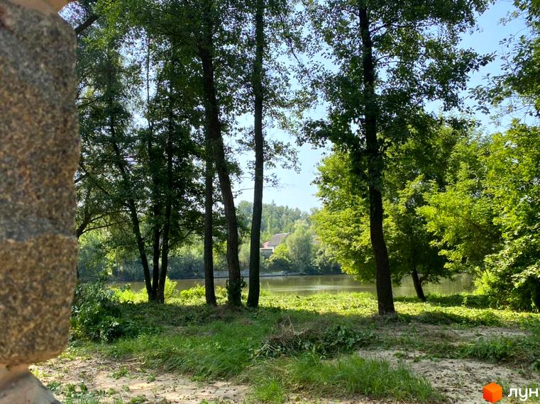 Будинок Котеджного містечка LAKESIDE OASIS на березі водойми, оточений густими деревами та зеленою територією.