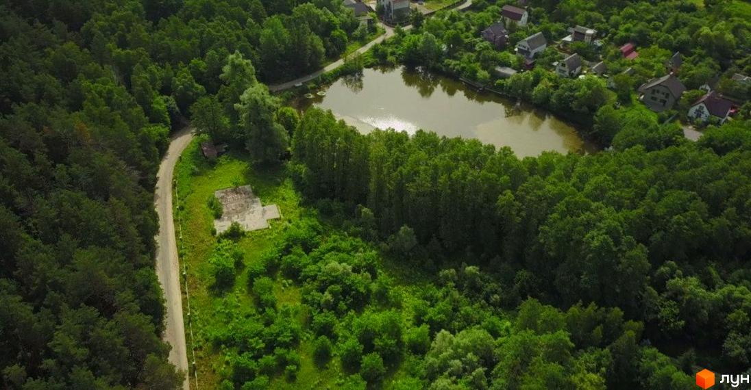 Вид з повітря на котеджне містечко LAKESIDE OASIS з озером та зеленою зоною. Навколо комплексу розташовані густі ліси та невеликі будиночки.