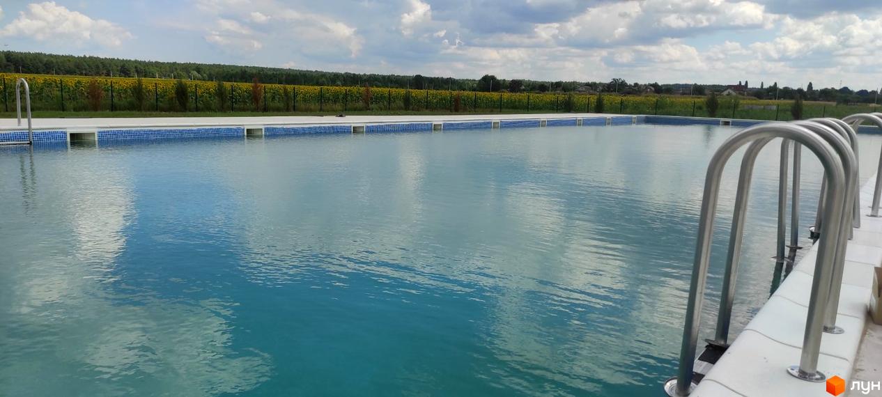 Житловий комплекс Лелека: відкритий басейн з блакитною водою та шезлонгами на тлі поля соняшників. На території комплексу є зелені насадження та дерева.