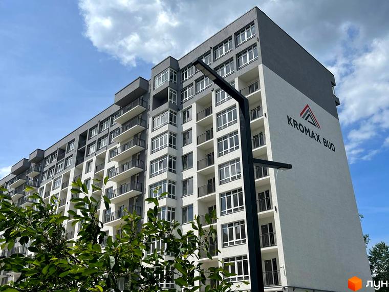Зовнішній вигляд новобудови ЖК Kromax Bud з балконами та великими вікнами під блакитним небом. На фасаді будівлі розміщено логотип компанії.