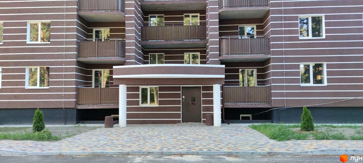 Зовнішній вигляд новобудови ЖК Парковий з коричневим фасадом та білими смугами, вікнами та балконами. Перед будинком викладена бруківка та зелені насадження.