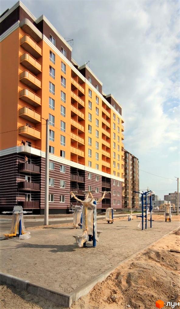 Житловий комплекс Парковий: яскрава фасадна частина будинку з балконами та прибудинкова територія зі спортивними тренажерами.