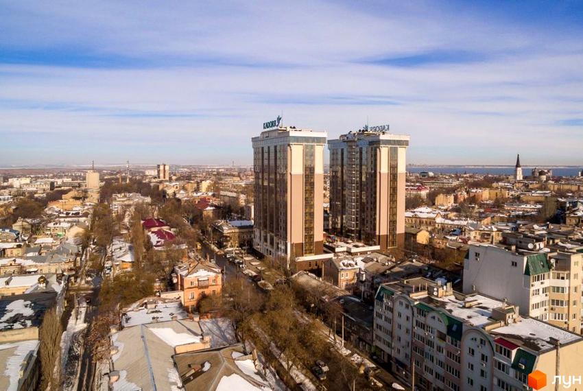 Високі будинки ЖК Шістнадцята Перлина в місті. Зверху видно напис на будівлях. Навколо будівель розташовані інші будинки та дерева.