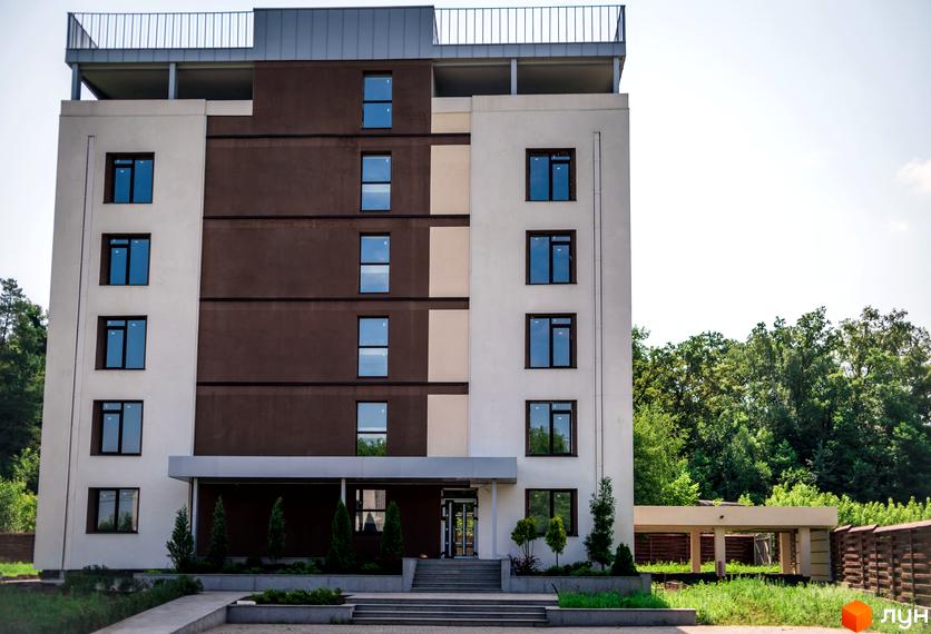 Зовнішній вигляд новобудови ЖК Summerville з коричнево-білим фасадом та вікнами. Навколо будинку зелена територія з деревами та парканом.