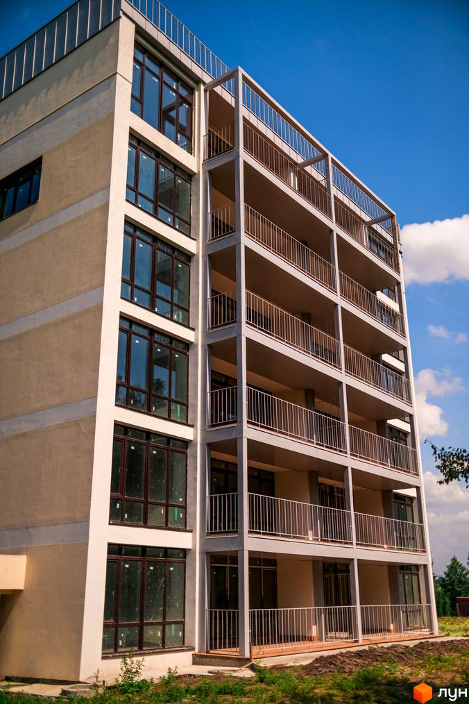 Зовнішній вигляд багатоквартирного будинку ЖК Summerville з балконами та великими вікнами на тлі блакитного неба. Навколо будинку облаштована прибудинкова територія з зеленими насадженнями.