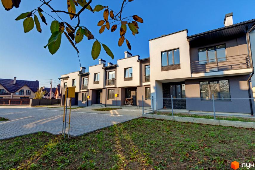 Ряд двоповерхових котеджів Котеджного містечка Grafit з фасадами світлих та темних відтінків. Перед будинками розташовані вимощені доріжки та зелені насадження.