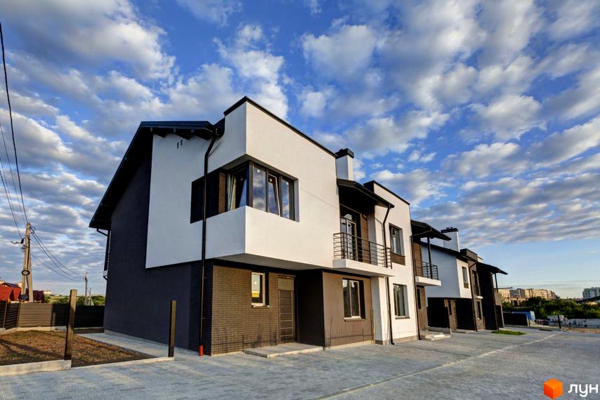 Ряд двоповерхових таунхаусів Котеджного містечка Grafit з білими та темно-сірими фасадами. Перед будинками вимощена територія.