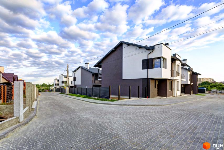 Котеджне містечко Grafit: двоповерхові будинки з білими та темно-сірими фасадами, що стоять уздовж вимощеної бруківкою дороги.