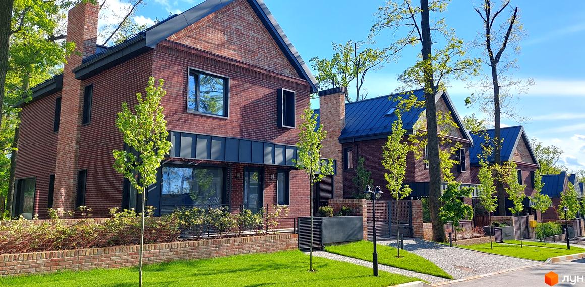 Цегляні будинки з темними дахами в котеджному містечку Oak Grove Town. На території є доглянутий газон, тротуари з бруківки та молоді дерева.