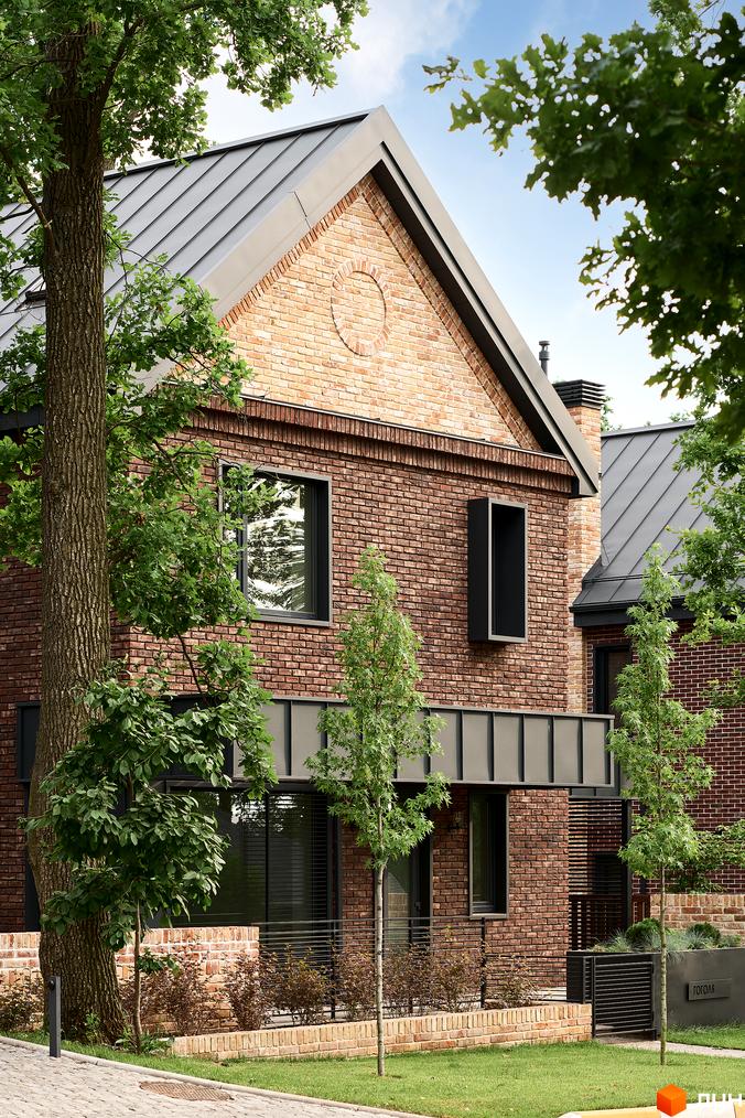 Зображення будинку в КМ Oak Grove Town з цегляним фасадом та металевим дахом. Поряд з будинком ростуть дерева, а також є невелика прибудинкова територія.