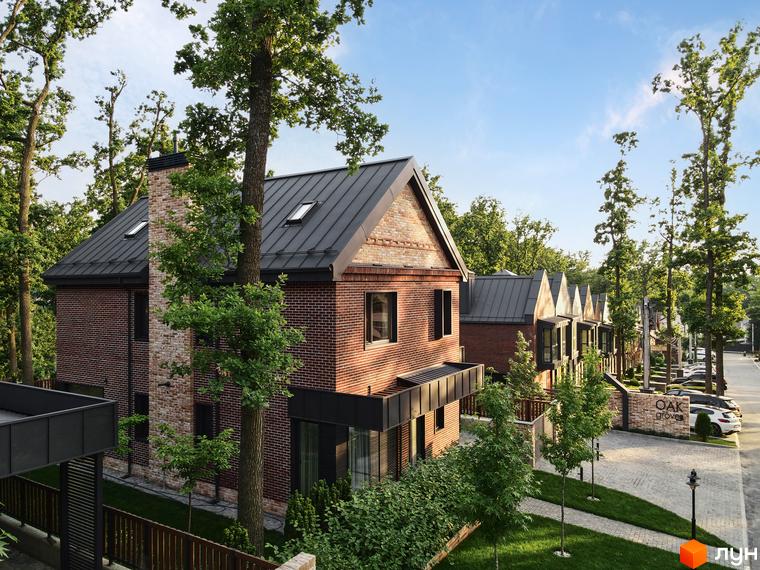 Цегляний будинок з темною покрівлею в котеджному містечку Oak Grove Town. На території комплексу є доріжки, газон та дерева.