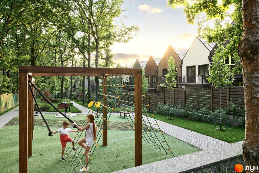 Дитячий майданчик у Містечку котеджів Oak Grove Town з сучасними будинками на задньому плані. На території є зелені насадження та доріжки.