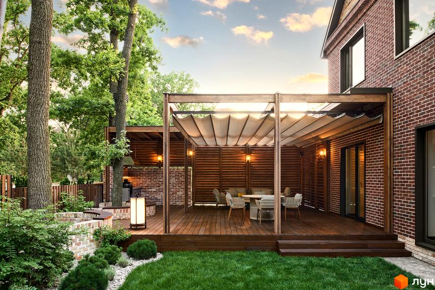 Котеджне містечко Oak Grove Town: Будинок з червоної цегли та простора дерев'яна тераса з навісом, оточена зеленим газоном.