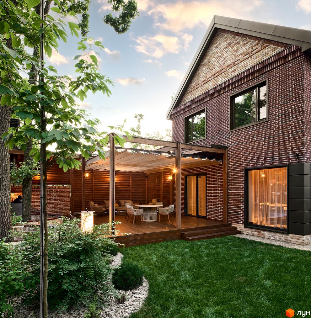 Цегляний будинок з великими вікнами та терасою. Зелена галявина перед будинком, дерева та кущі створюють затишну атмосферу. КМ Oak Grove Town.