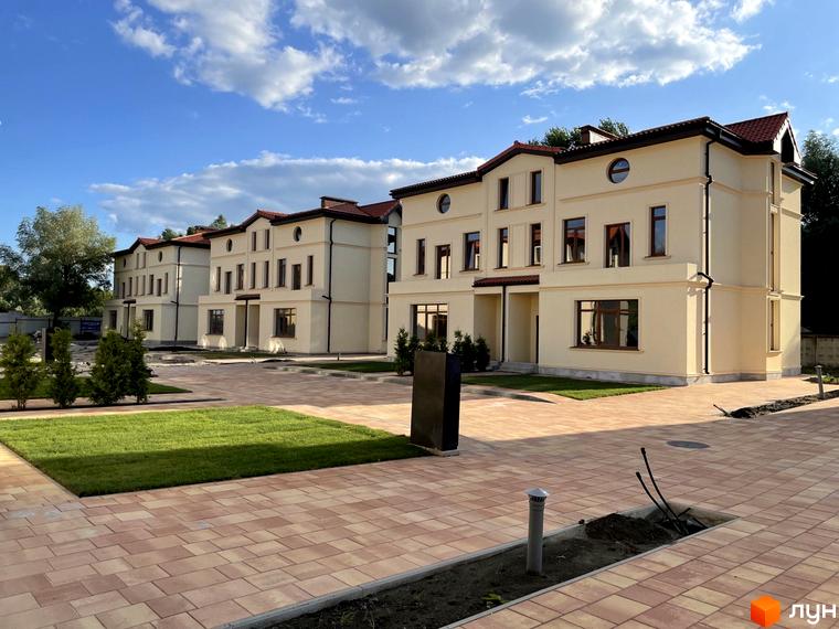 Котеджне містечко КМ Фонтан з фасадами світло-бежевого кольору та червоним дахом. Прибудинкова територія з бруківкою та зеленими газонами.