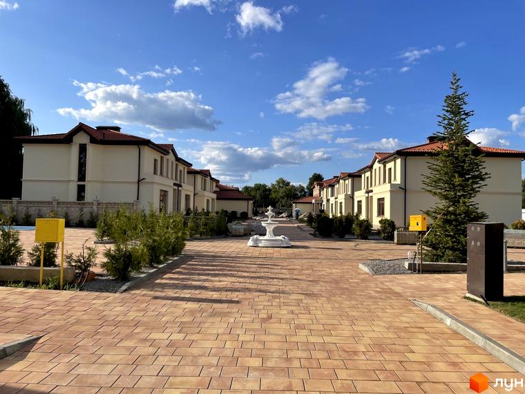 Котеджне містечко КМ Фонтан: світлі фасади будинків з червоним дахом та доглянута прибудинкова територія з бруківкою та зеленими насадженнями.