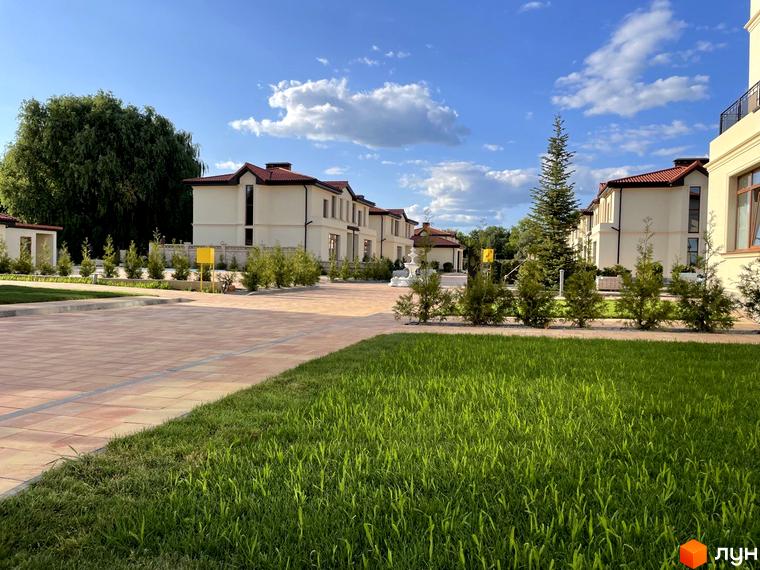 Котеджне містечко КМ Фонтан: двоповерхові будинки з червоними дахами та зеленою прибудинковою територією. Акуратні доріжки та доглянутий газон створюють затишну атмосферу.