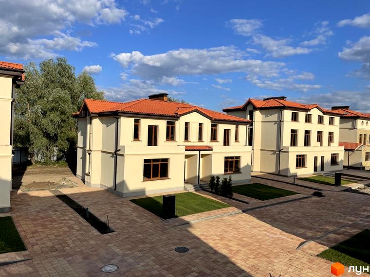 Котеджне містечко КМ Фонтан: двоповерхові будинки світло-бежевого кольору з червоними черепичними дахами, брукована прибудинкова територія з зеленими газонами.