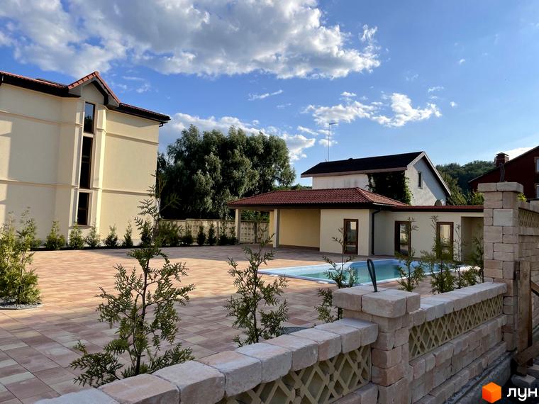 Котеджне містечко КМ Фонтан: триповерхова будівля світло-бежевого кольору з червоним дахом, поруч басейн та зелені насадження.