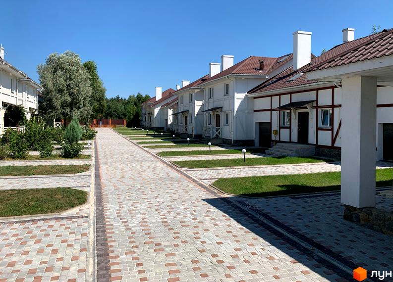 Зображення Котеджного містечка „Северинівська Перлина“: двоповерхові будинки з коричневими дахами та світлими стінами, між будинками викладена тротуарна плитка.