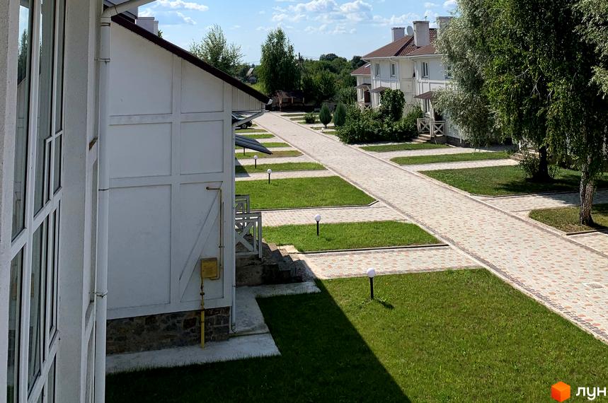 Зображення Котеджного містечка „Северинівська Перлина“: білі котеджі з коричневими дахами, акуратні газони та доріжки з тротуарної плитки.