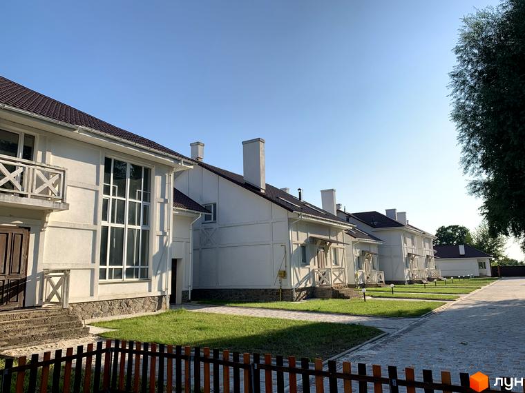 Зображення Котеджного містечка „Северинівська Перлина“: двоповерхові будинки з коричневими дахами та великими вікнами. Навколо будинків зелені газони та доріжки.