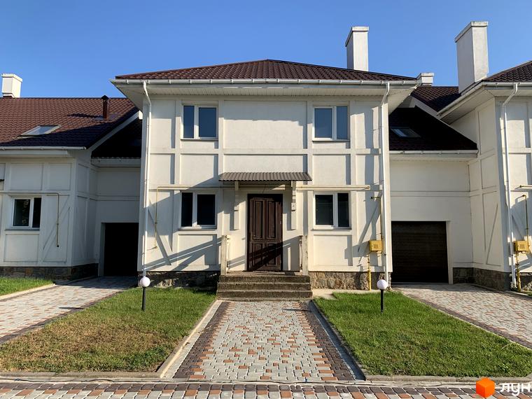 Зовнішній вигляд будинку в Котеджному містечку „Северинівська Перлина“. Двоповерховий будинок з коричневим дахом та білими стінами, перед будинком доріжка з бруківки.