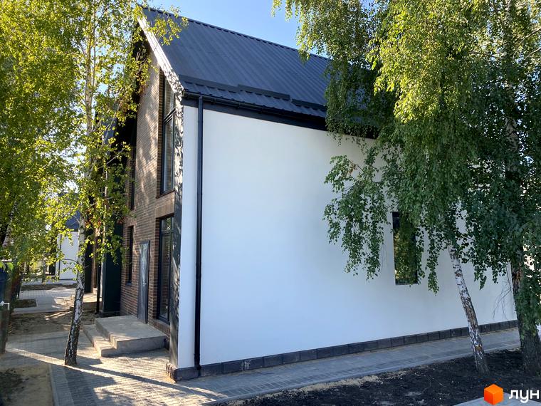 Зовнішній вигляд дуплексів „Тут“ з цегляним фасадом та білою штукатуркою, прибудинкова територія з бруківкою та деревами.