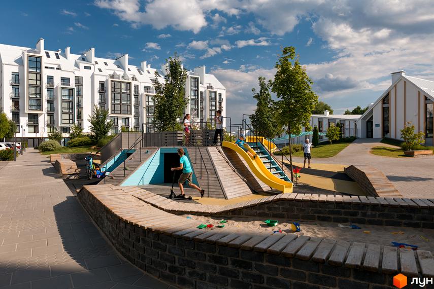 Фото Житлового комплексу City Lake з дитячим майданчиком. На фоні білі багатоповерхівки з великими вікнами та зелені насадження.