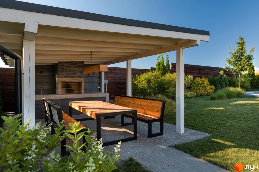 КМ VILLAGGO – котеджне містечко з зоною барбекю та обідньою групою під навісом. Зелена доглянута територія з газоном та кущами.