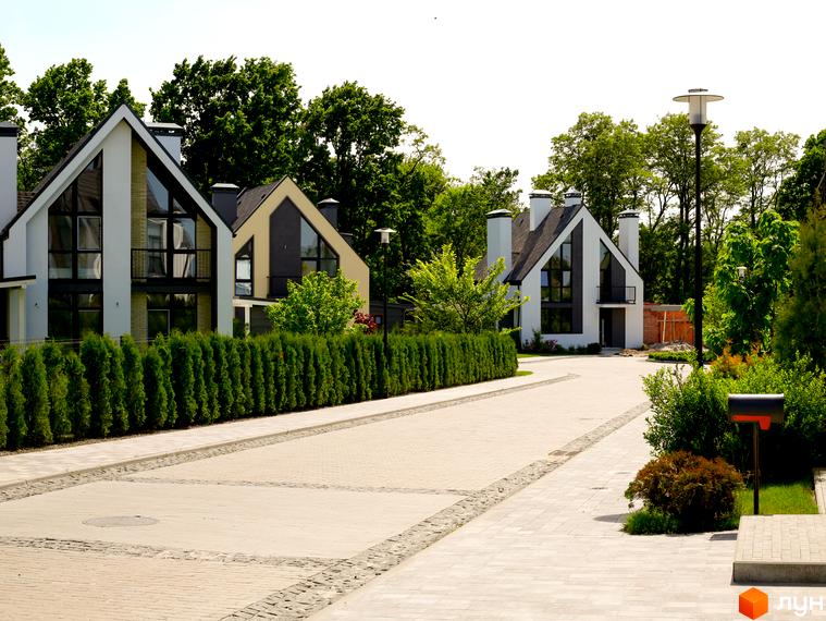 Котеджне містечко КМ VILLAGGO: сучасні будинки з великими вікнами та доглянутою територією. Асфальтована дорога веде до котеджів, оточених зеленню.