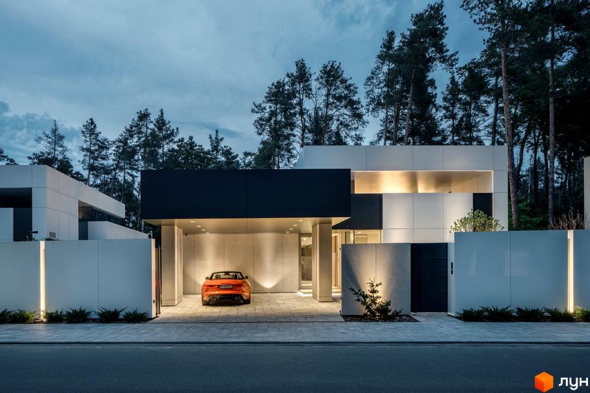 Будинок Котеджного містечка 3L Residences з чорно-білими фасадами та освітленням. Перед ним вимощена ділянка з автомобілем та огорожею, оточена лісом.