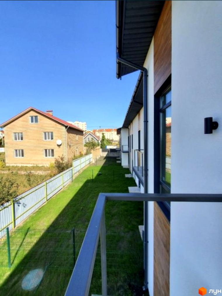 Таунхаус Blestown з цегляним фасадом та червоним дахом, зелена галявина та паркан біля будинку.