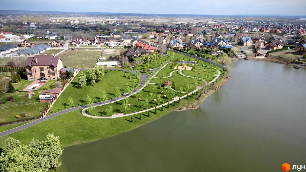 Котеджне містечко Зоряний: двоповерхові будинки з коричневими дахами, зелена прибудинкова територія з алеями та місцями для відпочинку біля озера.
