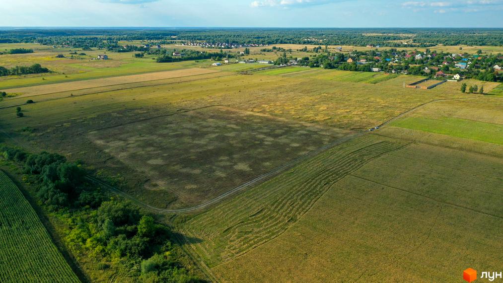Котеджне містечко Луговий - вид з висоти пташиного польоту на зелені поля та житлові будинки. Навколо комплексу розташовані поля та лісосмуги.