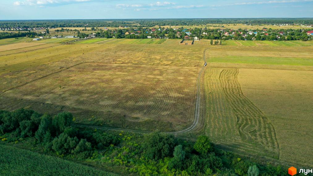 Котеджне містечко КМ Луговий: мальовничі поля та зелені насадження навколо житлових будинків. Вид з висоти пташиного польоту на забудову та сільську місцевість.