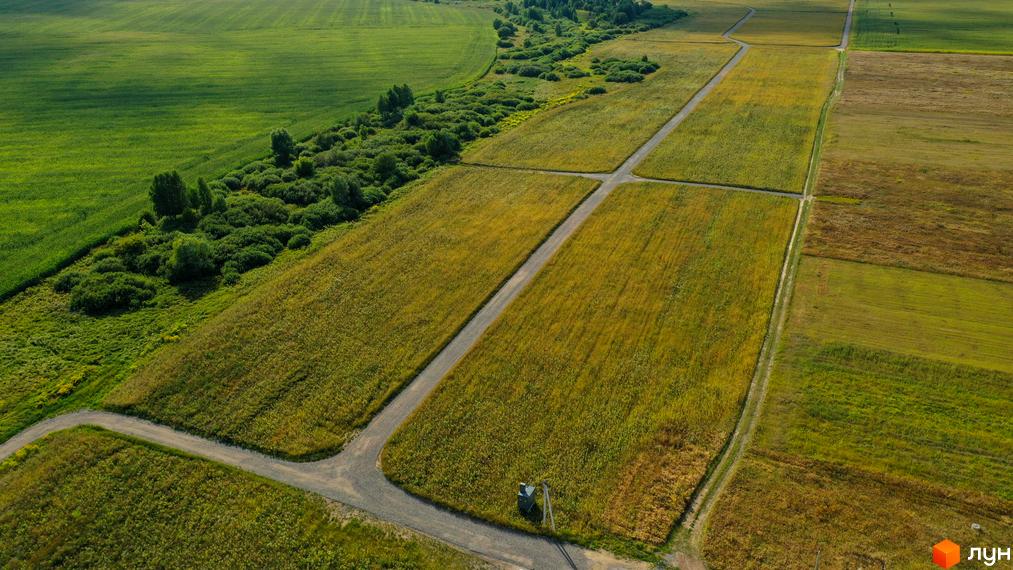 Зображення Котеджного кварталу „Фортеця Колонщини“ з висоти пташиного польоту. Видно поля, дерева та дороги, що ведуть до будинків.