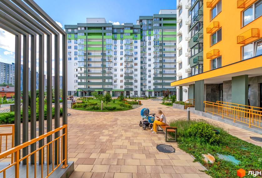 Зовнішній вигляд ЖК Сирецькі сади з яскравими фасадами та зеленою прибудинковою територією. На території комплексу розташовані лавочки та дитячий майданчик.