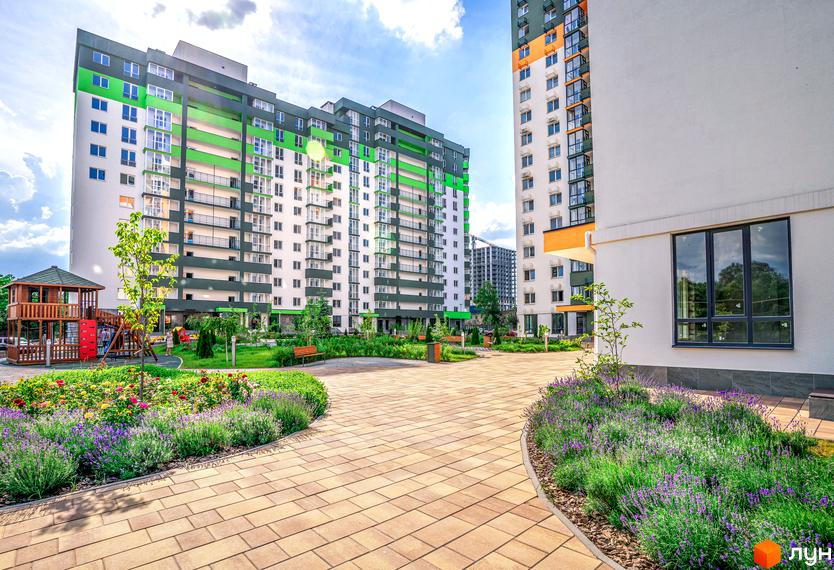 Житловий комплекс Сирецькі сади. Фасади будівель з зеленими та білими елементами, облаштований двір з дитячим майданчиком та квітучими клумбами.