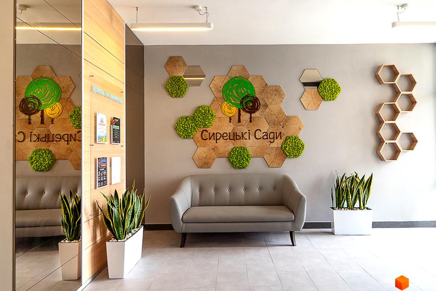 Житловий комплекс Сирецькі сади. Інтер'єр зони очікування з диваном та рослинами, декорований елементами з дерева та моху.