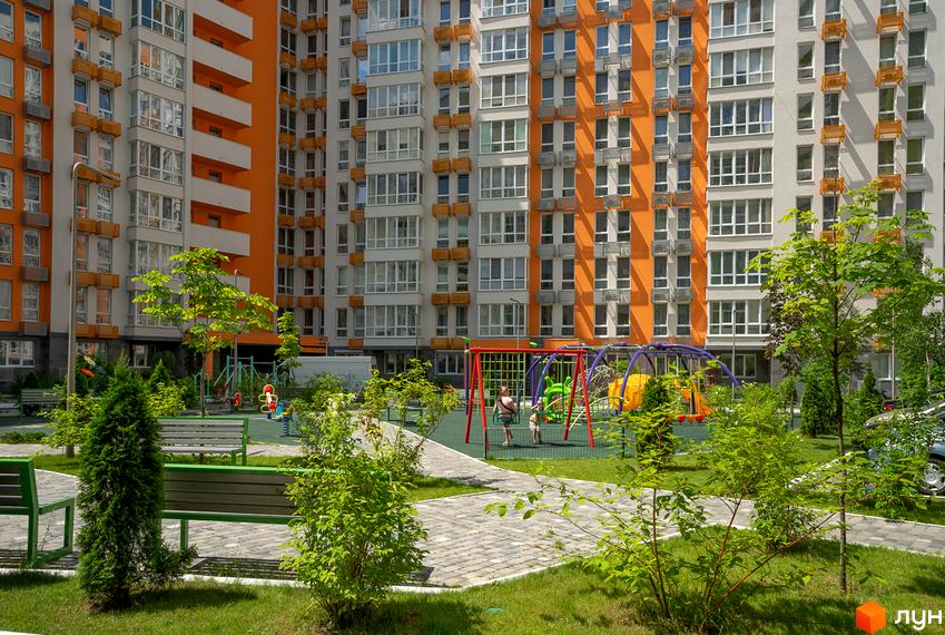 Високоповерховий будинок житлового комплексу Нивки-Парк з яскравим фасадом. На території комплексу дитячий майданчик та зелені насадження.