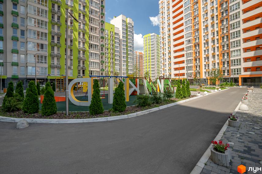 Високі будинки житлового комплексу Нивки-Парк з яскравими фасадами. На території комплексу є дитячий майданчик та доглянуті алеї.
