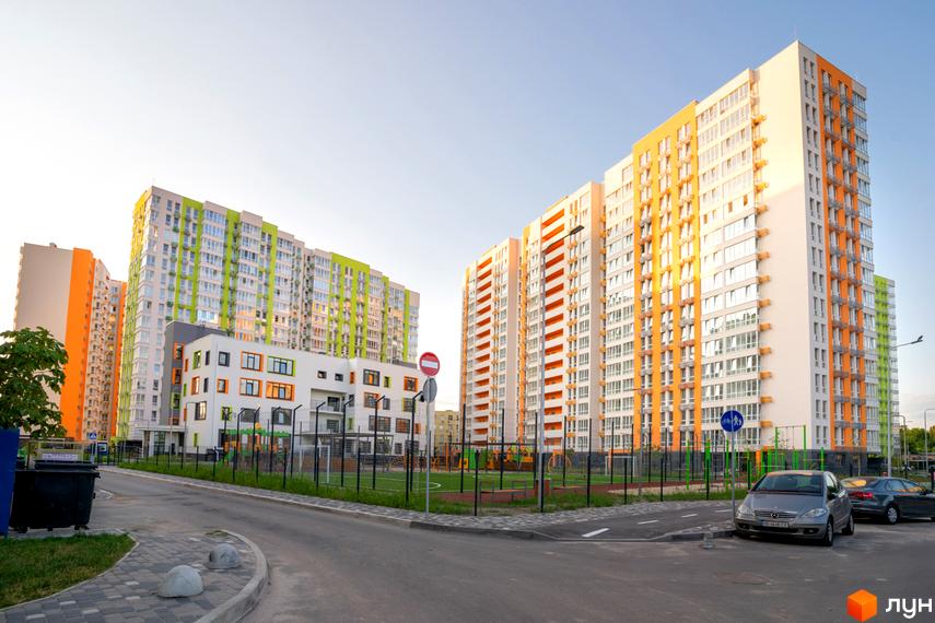 Житловий комплекс Нивки-Парк. Високі будинки з помаранчевими та зеленими акцентами на фасадах. На території комплексу є дитячий майданчик та парковка.