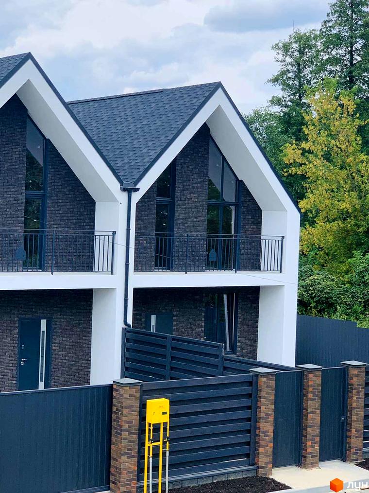 Двоповерховий будинок з темно-сірою цегляною кладкою та білими акцентами. На території розташований паркан з цегляними стовпчиками.