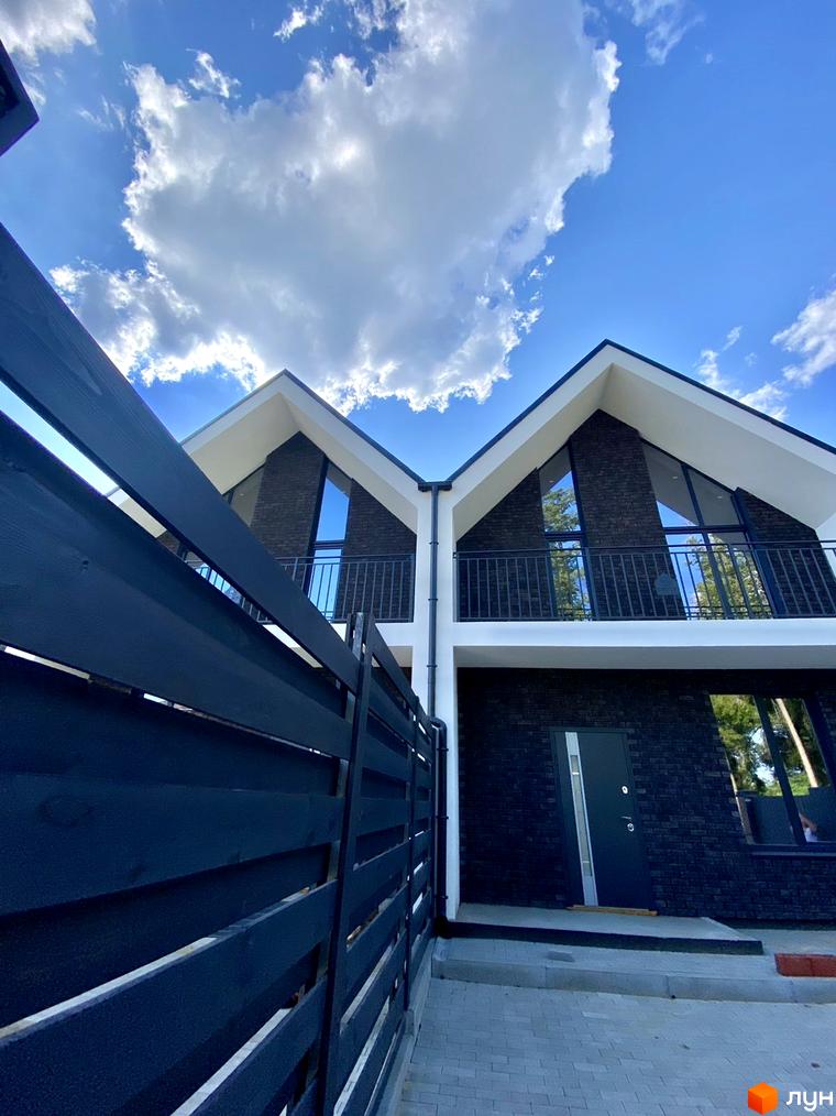 Дуплекс MANHATTAN з темною цегляною облицовкою та великими вікнами під блакитним небом. Огороджена територія з дерев'яним парканом.