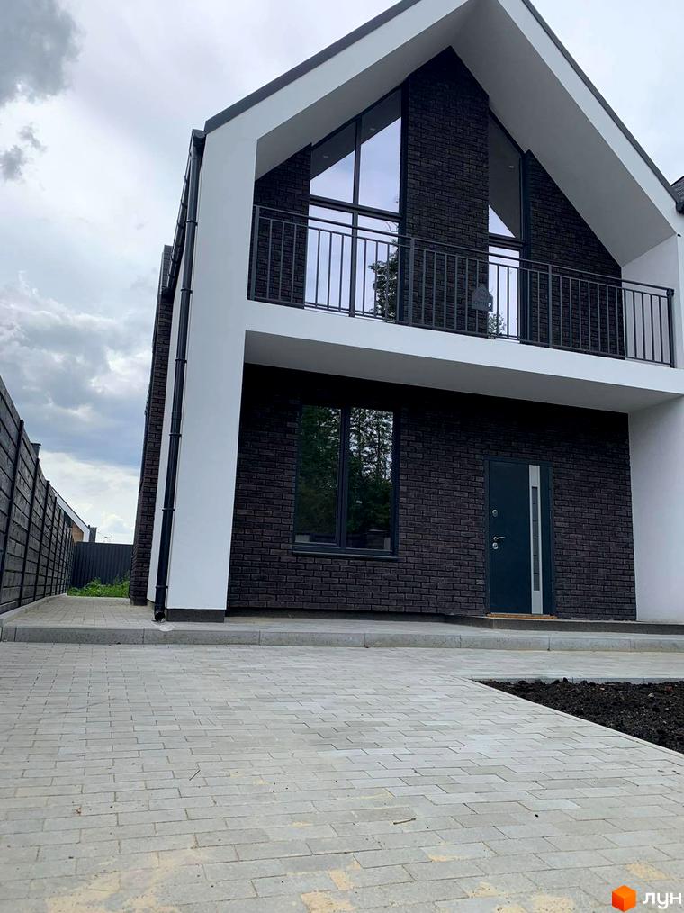 Двоповерховий будинок з темної цегли з великими вікнами та балконом. Перед будинком викладена бруківка.