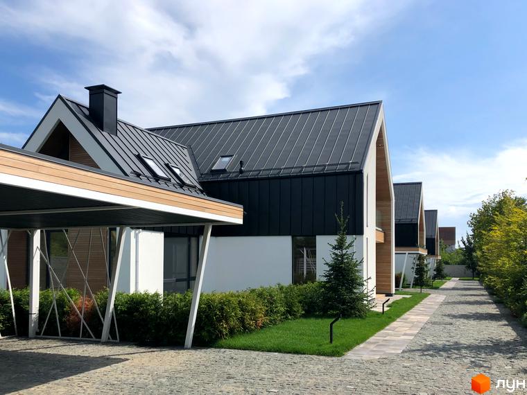 Котеджне містечко КМ Hill Park: фасади будинків з темним металевим дахом та дерев'яними елементами, вимощені доріжки та зелені насадження.