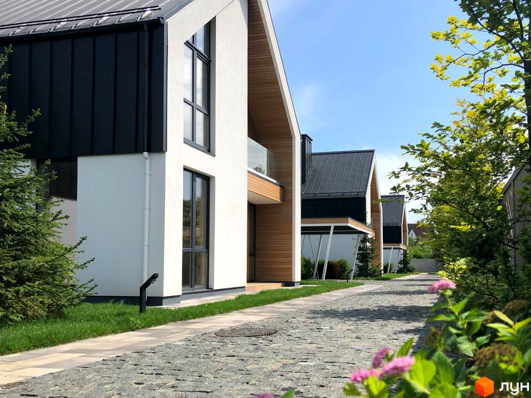 Котеджне містечко КМ Hill Park. Зовнішній вигляд будинків з чорними дахами та білими стінами, вимощена дорога та зелені насадження.