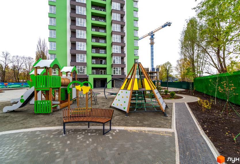 Зображення будинку та дитячого майданчика в Житловому комплексі Академ-Квартал. На фото багатоповерхівка з ігровим майданчиком для дітей.